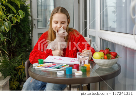 Lovely child girl painting and sitting with cat pet on the terrace. 137241331
