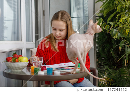 Attractive child girl painting and sitting with cat pet on the terrace. Kid 11 years old 137241332