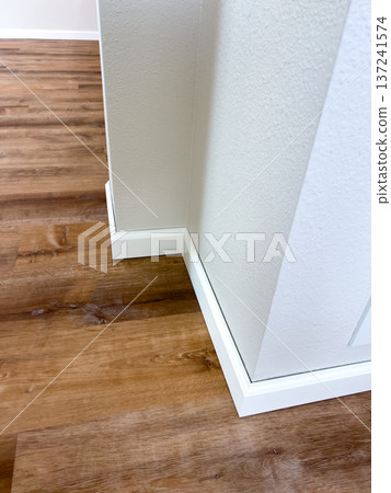 Corner view showing crisp white baseboards paired with natural-looking vinyl floors. Perfect for advertising flooring products, home renovation inspiration, or interior design blogs. 137241574