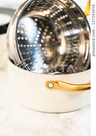 Stainless steel steamer insert nested inside a white pot with golden handles, shown in a vertical format. Ideal for kitchenware catalogues and product detail shots. Stainless steel steamer insert nested inside a white pot with golden handles, shown in a vertical format. Ideal for kitchenware catalogues and product detail shots. 137241658