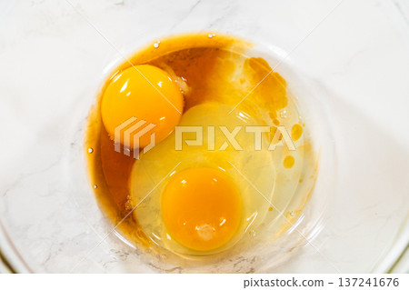 Close overhead view of eggs and liquid ingredients mixed lightly in a glass bowl. Bright lighting emphasizes color contrast and clean baking environment. 137241676