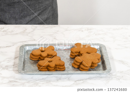 Gingerbread cookies, including a gingerbread man with a heart-shaped cutout, rest on a rustic metal tray against a marble countertop. 137241680