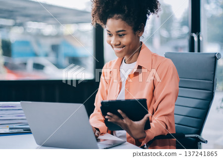 Smiling businesswoman working on laptop in office Smiling businesswoman working on laptop in office 137241865