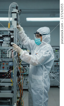 A scientist adjusts tall industrial laboratory equipment inside a clean facility. Bright lighting highlights complex wiring and components. The atmosphere is technical and precise. A scientist adjusts tall industrial laboratory equipment inside a clean facility. Bright lighting highlights complex wiring and components. The atmosphere is technical and precise. 137242055