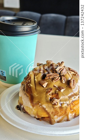 Caramel pecan cinnamon roll with coffee cup on table in cafe interior. Sweet breakfast pastry and hot drink symbolizing indulgence, comfort and morning ritual concept Caramel pecan cinnamon roll with coffee cup on table in cafe interior. Sweet breakfast pastry and hot drink symbolizing indulgence, comfort and morning ritual concept 137242432