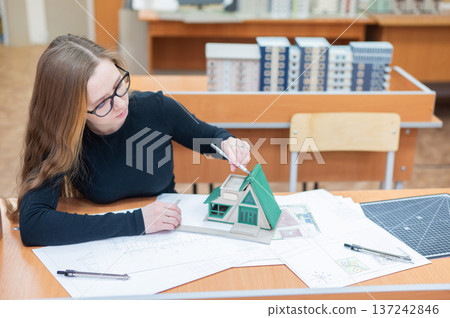 Caucasian young woman making a model of a building. Student of the construction university. Caucasian young woman making a model of a building. Student of the construction university. 137242846