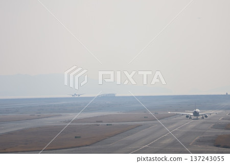 機場景色,一架飛機正在準備降落,另一架飛機正在跑道上滑行,天空和大海都籠罩在薄霧之中。 機場景色,一架飛機正在準備降落,另一架飛機正在跑道上滑行,天空和大海都籠罩在薄霧之中。 137243055
