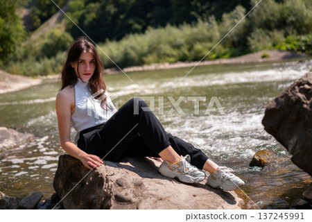 Relaxed Young Woman Resting on Rocks by a Mountain River Relaxed Young Woman Resting on Rocks by a Mountain River 137245991