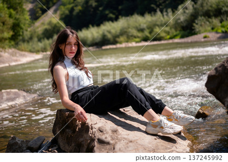 Relaxed Young Woman Resting on Rocks by a Mountain River Relaxed Young Woman Resting on Rocks by a Mountain River 137245992