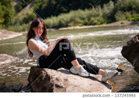 Relaxed Young Woman Resting on Rocks by a Mountain River Relaxed Young Woman Resting on Rocks by a Mountain River 137245993