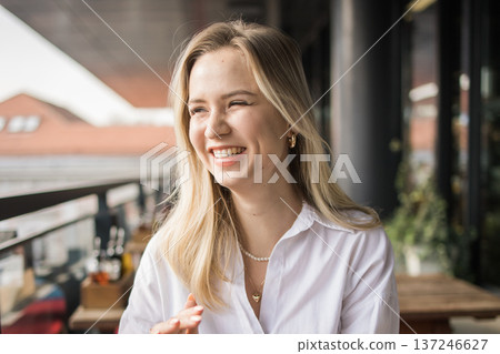 Laughing woman sitting on a cafe terrace enjoying a cheerful conversation. Happiness, friendship, urban social life, communication and joyful everyday moments in the city. 137246627