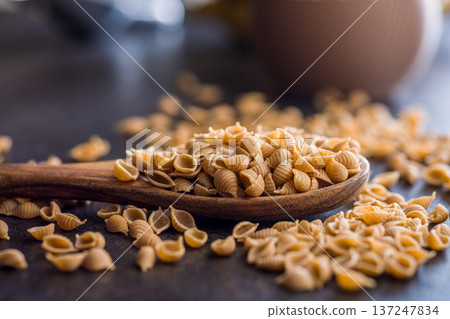 Wholegrain conchiglie pasta on spoon on black table. Wholegrain conchiglie pasta on spoon on black table. 137247834