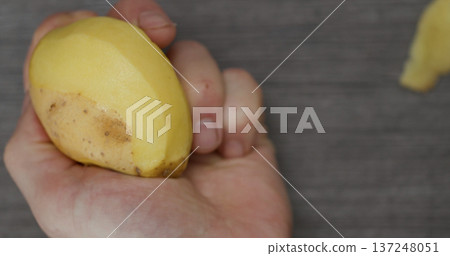 Holding a fresh yellow potato with a hand above a gray surface during a kitchen preparation activity Holding a fresh yellow potato with a hand above a gray surface during a kitchen preparation activity 137248051