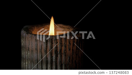 Candle burns brightly in dark setting creating warm glow and gentle light during quiet evening hours 137248083