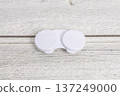 A white contact lens case placed on a wood grain background 137249000