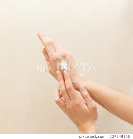 Close up hands of woman applying white moisturizing cream to the back of her hand, symbolizing natural skin care, hydration, beauty, and health rituals for soft, smooth, and nourished skin 137249106