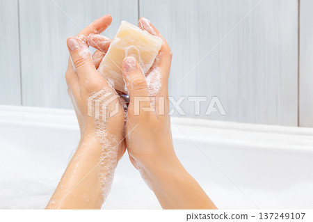 Hands lathering a bar of soap, creating white foam and bubbles over a white ceramic sink, emphasizing personal hygiene, cleanliness, and daily hand washing routine for health and skincare 137249107