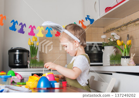 Toddler Painting Easter Eggs at Home in Festive Kitchen Toddler Painting Easter Eggs at Home in Festive Kitchen 137249202