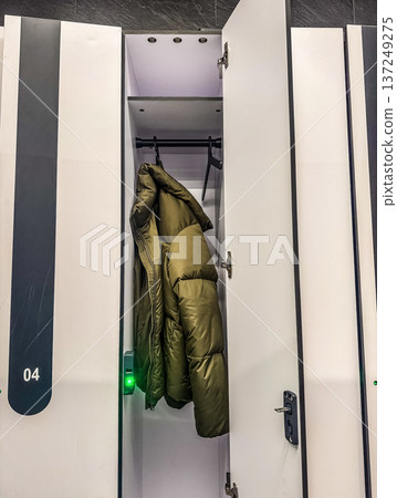Open locker with a green puffer jacket hanging inside. Modern gym or office changing room with secure electronic locks. 137249275