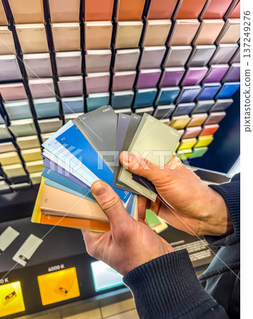 Man's hands selecting paint color swatches from a sample fan deck. Choosing a palette for interior design or home renovation. Man's hands selecting paint color swatches from a sample fan deck. Choosing a palette for interior design or home renovation. 137249276