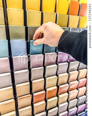 Man's hand choosing a blue paint color swatch from a display rack. Interior design and home renovation concept. Man's hand choosing a blue paint color swatch from a display rack. Interior design and home renovation concept. 137249281