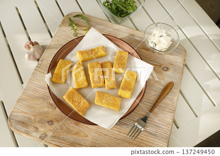 Sliced pieces of fried hard polenta on plate on table. Cornmeal in kitchen. Ingredients and traditional Italian cuisine. Sliced pieces of fried hard polenta on plate on table. Cornmeal in kitchen. Ingredients and traditional Italian cuisine. 137249450