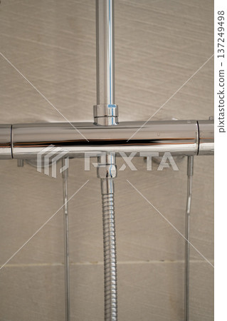 Chrome shower mixer faucet with a flexible hose connecting to the main pipe and a vertical riser, showcasing modern interior design in a bathroom with light beige tiles 137249498