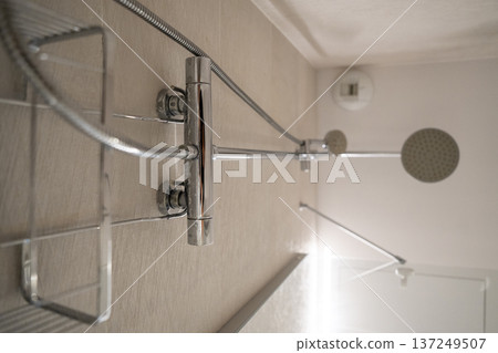 Modern bathroom shower system featuring a large rainfall shower head, handheld shower, and chrome fixtures with a soap rack and mixer valve 137249507