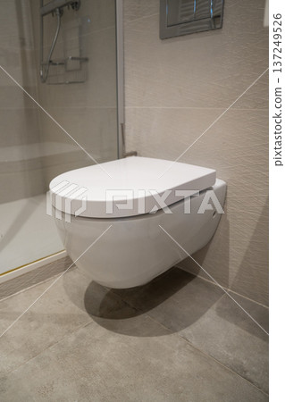 Modern bathroom interior showing a clean white wall-hung toilet with a closed lid, integrated into contemporary tiled decor, focusing on hygiene, luxury, and design Modern bathroom interior showing a clean white wall-hung toilet with a closed lid, integrated into contemporary tiled decor, focusing on hygiene, luxury, and design 137249526