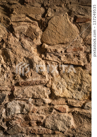 Ancient stone wall showcasing a rough, textured surface with varying rock types and visible mortar, highlighting durability and historical construction 137249535