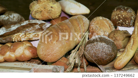 Fresh baked bread displayed on a wooden table in a bakery during daytime with various types of bread visible Fresh baked bread displayed on a wooden table in a bakery during daytime with various types of bread visible 137249662