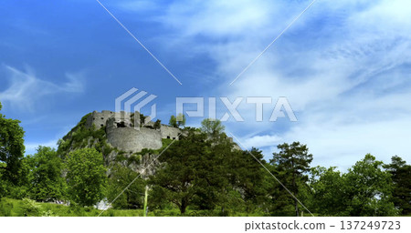 Visitors explore the ancient castle on a hill surrounded by green trees under a clear blue sky in springtime Visitors explore the ancient castle on a hill surrounded by green trees under a clear blue sky in springtime 137249723