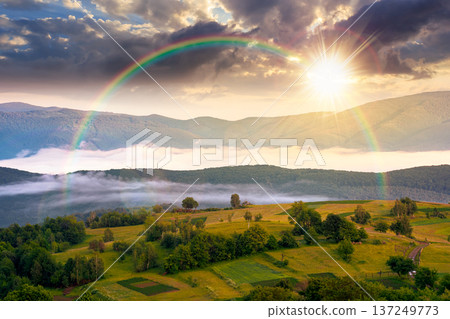sunset over mountainous rural area during springtime. remote mountain landscape with forested rolling hills. wonderful foggy place of alpine countryside wallpaper. weather with rainbow 137249773