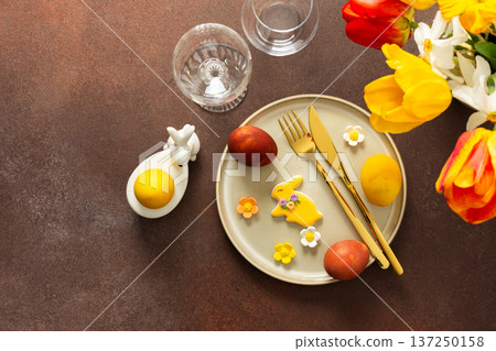 A beautifully arranged Easter table displays vibrant eggs, elegant gold cutlery, and a lively bouquet of tulips and lilies. This setting creates a cheerful atmosphere for the holiday feast A beautifully arranged Easter table displays vibrant eggs, elegant gold cutlery, and a lively bouquet of tulips and lilies. This setting creates a cheerful atmosphere for the holiday feast 137250158