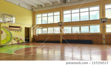 An empty indoor basketball court in a school gymnasium with a wooden floor and hoops. The bright interior of the gymnasium symbolizes education, training, competition, and a healthy lifestyle An empty indoor basketball court in a school gymnasium with a wooden floor and hoops. The bright interior of the gymnasium symbolizes education, training, competition, and a healthy lifestyle 137250517
