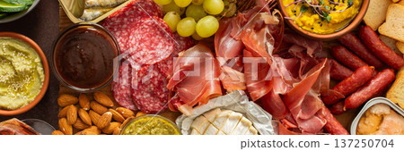 Taste a variety of flavors with this charcuterie board filled with cheese, sausages, hummus, nuts, and fresh sandwiches, perfect for any gathering, banner 137250704