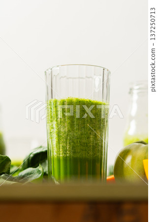 Fresh juice is made using spinach, chard, and broccoli along with oranges and tangerines. A glass of green juice sits by fresh ingredients on a clean kitchen counter 137250713
