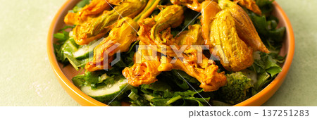 Roasted zucchini flowers are placed on a bed of fresh greens, cucumbers, and broccoli during a summer meal. This dish highlights the flavors of summer ingredients, banner Roasted zucchini flowers are placed on a bed of fresh greens, cucumbers, and broccoli during a summer meal. This dish highlights the flavors of summer ingredients, banner 137251283
