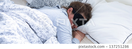 A middle-aged woman is sleeping soundly in her bed, wearing a sleep mask. She is surrounded by soft pillows and a warm blanket, taking a break from her daily routine, banner A middle-aged woman is sleeping soundly in her bed, wearing a sleep mask. She is surrounded by soft pillows and a warm blanket, taking a break from her daily routine, banner 137251286