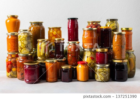 Canned vegetables and fruits are stacked on a shelf, prepared for winter use. Various jars hold different preserves, showcasing careful efforts for storing food during the season 137251390