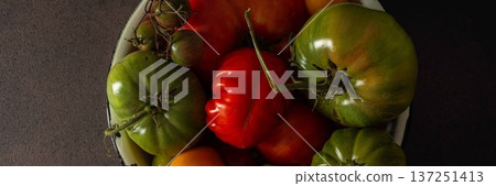 A bowl holds a variety of fresh tomatoes, showing different colors and sizes. The setting features a dark background that highlights the tomatoes in natural light, banner A bowl holds a variety of fresh tomatoes, showing different colors and sizes. The setting features a dark background that highlights the tomatoes in natural light, banner 137251413