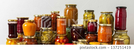 Canned vegetables and fruits are stacked on a shelf, prepared for winter use. Various jars hold different preserves, showcasing careful efforts for storing food during the season, banner 137251419