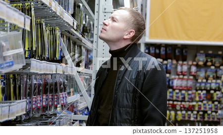 Man carefully choosing a drill bit in a busy hardware store, surrounded by tools and supplies for diy projects and home improvement. A man in a hardware store choosing a tool. Man carefully choosing a drill bit in a busy hardware store, surrounded by tools and supplies for diy projects and home improvement. A man in a hardware store choosing a tool. 137251958