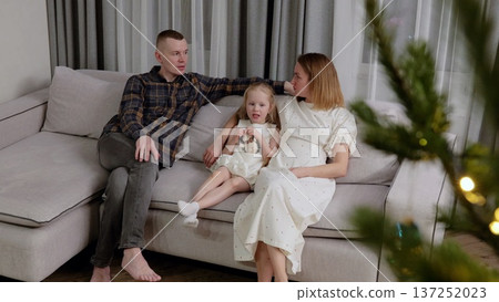 Pregnant woman relaxing with partner and child on festive sofa, enjoying warm family connection during holiday season, sharing tender moments and cheerful smiles Pregnant woman relaxing with partner and child on festive sofa, enjoying warm family connection during holiday season, sharing tender moments and cheerful smiles 137252023