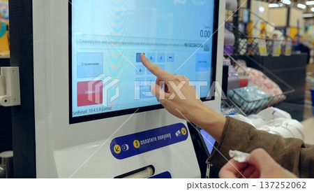 Customer at self service checkout kiosk entering pin code and holding shopping receipt in modern supermarket 137252062