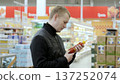 Man carefully examines the ingredients of hot sauce bottles while shopping in a grocery store, comparing various brands and flavors before deciding on a purchase 137252074