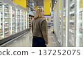 Young woman browsing refrigerated dairy products in a supermarket aisle, selecting groceries for her family 137252075