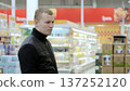 Focused man choosing food in supermarket aisle, emphasizing healthy eating and nutrition in lifestyle. A man studies the label on a bottle of sauce 137252120