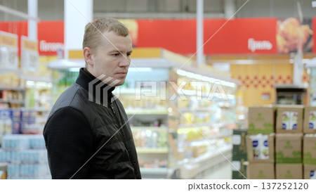 Focused man choosing food in supermarket aisle, emphasizing healthy eating and nutrition in lifestyle. A man studies the label on a bottle of sauce Focused man choosing food in supermarket aisle, emphasizing healthy eating and nutrition in lifestyle. A man studies the label on a bottle of sauce 137252120