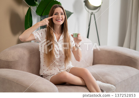 Happy young woman applying moisturizing cream on her face Happy young woman applying moisturizing cream on her face 137252853